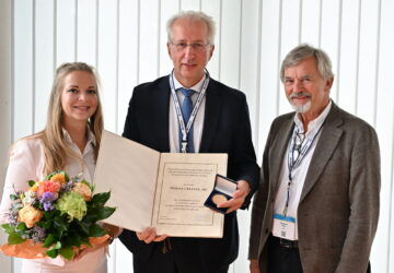 Prof. Dr. Tomasz Urbanek, Gefäßchirurg an der Medizinischen Universität Schlesien in Katowice, steht mit Urkunde und Medaille zwischen zwei Personen. Links hält Michelle Schaub einen Blumenstrauß, rechts steht Prof. Eberhard Rabe. Die Auszeichnung ist die Max-Ratschow-Gedächtnismedaille.